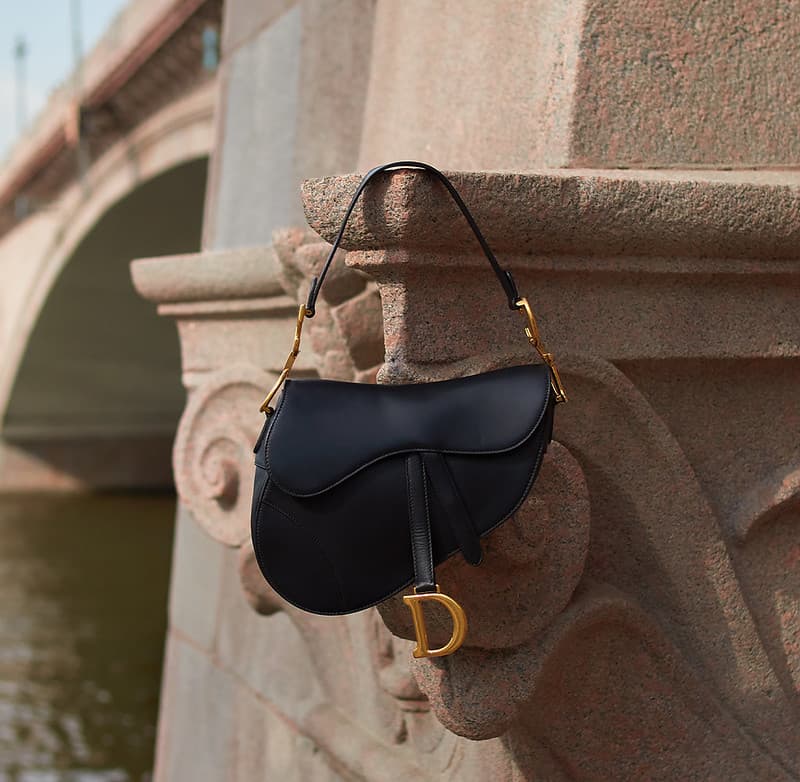 Black Dior Saddle bag hanging against a stone bridge in Paris, used as the featured image for an article about luxury resale myths, provenance, and secondhand value.